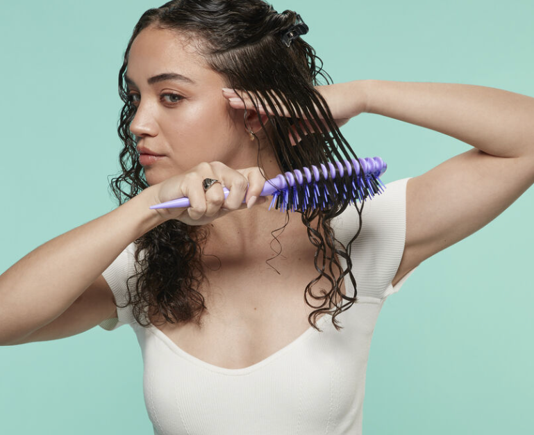 Woman brushing her hair with a purple brush against a light green background